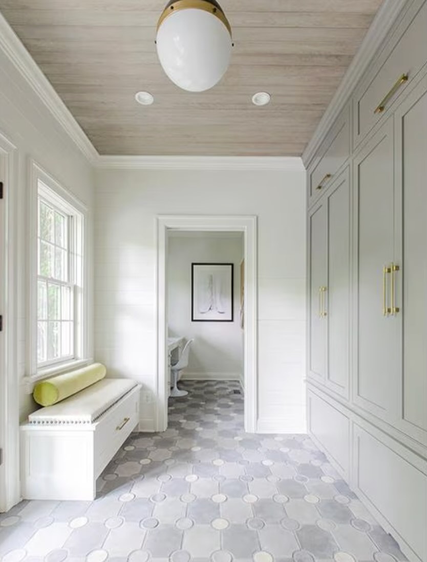 Bright mudroom with built-in cabinets, bench seating, patterned tile floor, and natural light from a window