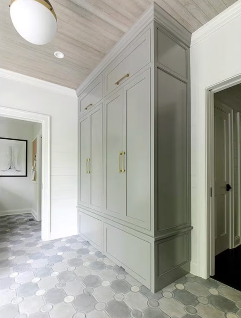 Built-in gray storage cabinets with brass handles in a bright mudroom with patterned tile flooring